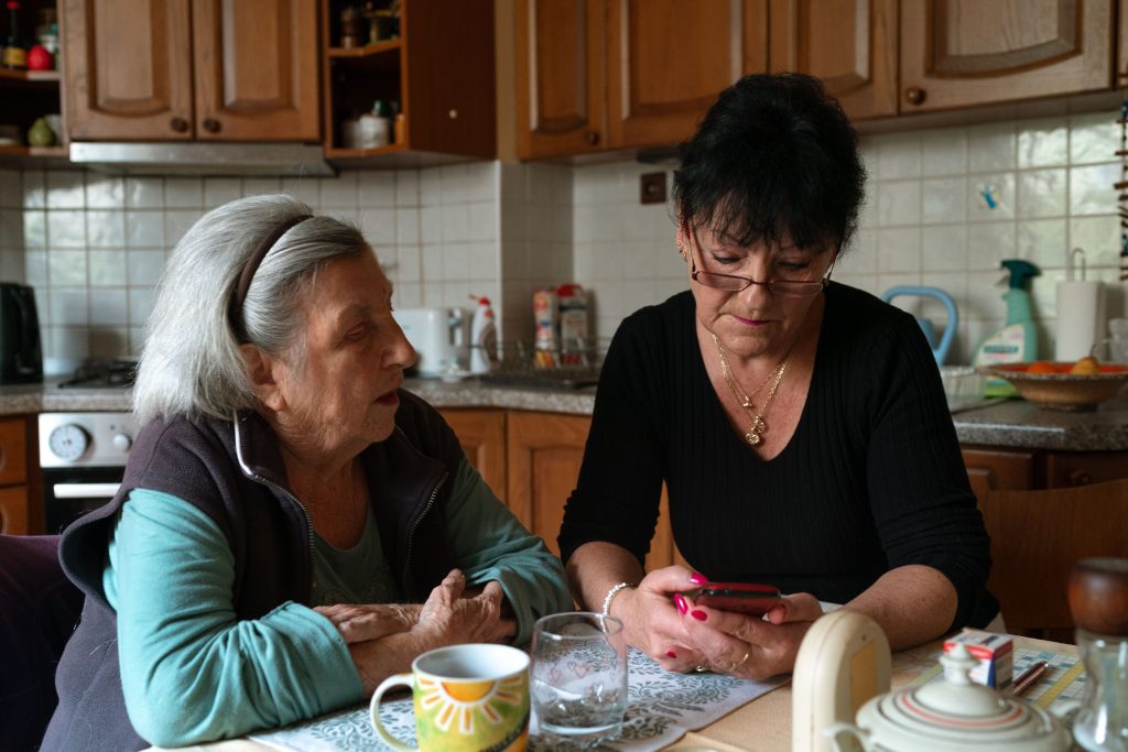 Adult daughter helping an older parent review information on a smartphone at home