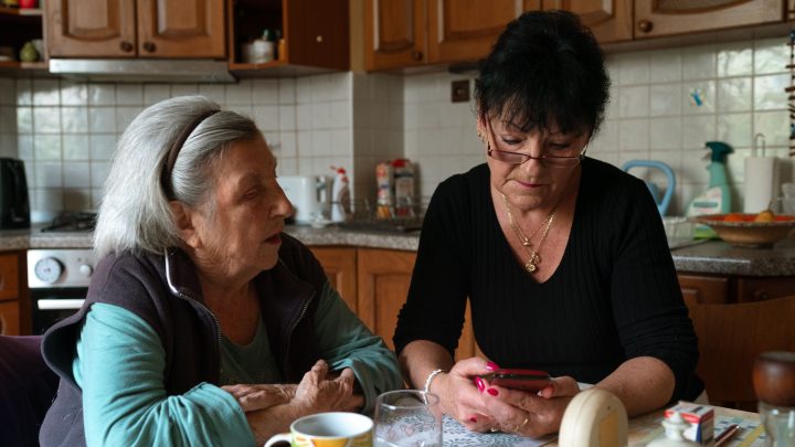 Adult daughter helping an older parent review information on a smartphone at home